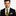 Man wearing a black suit with a yellow and black patterned tie and pocket square on a white background