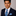 Man wearing a dark suit with a blue patterned tie and pocket square on a gray background