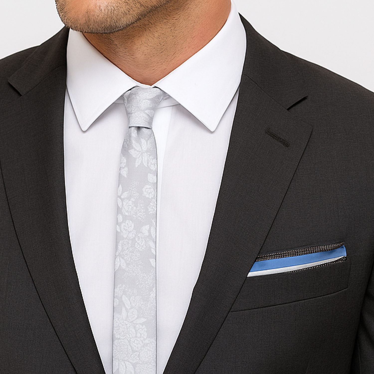 Man wearing a black suit with a white shirt, light gray tie, and blue pocket square.