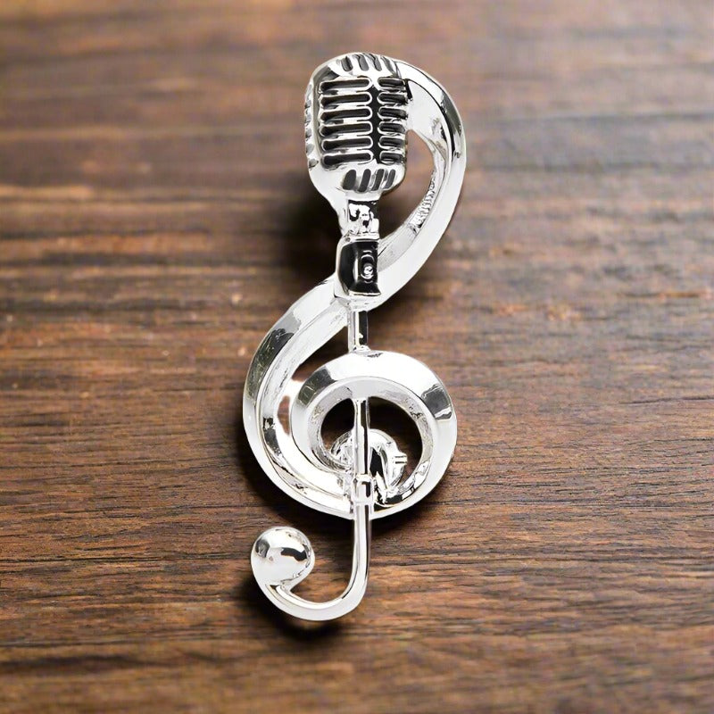 A Silver Colored Lapel Pin Shaped Like A Music Note With A Microphone