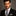 Man wearing a black suit with a patterned tie and pocket square on a gray background