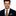 Man wearing a dark suit with a gold tie and pocket square on a white background