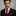 Man wearing a black suit with a red tie and pocket square on a gray background