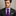 Man wearing a dark suit with a purple striped tie against a neutral background
