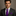 Man wearing a dark suit with a purple tie and pocket square against a neutral background