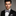 Man wearing a black suit with a white shirt and patterned bow tie on a gray background