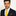 Man wearing a black suit with a yellow tie and white shirt on a light gray background
