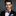 Man wearing a black suit with a purple bow tie and pocket square on a gray background