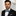 Man wearing a black suit with a blue bow tie and pocket square against a light background