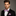 Man wearing a black suit with a purple bow tie and matching pocket square against a gray background
