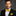 Man wearing a black suit with a yellow bow tie and pocket square on a gray background