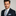 Man wearing a navy suit with a blue and white striped tie and pocket square on a gray background