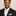 Man wearing a black suit with a beige tie and pocket square against a beige background