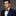 Man wearing a navy suit with a blue bow tie and pocket square on a gray background