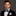 Man wearing a black suit with a blue bow tie and patterned pocket square on a gray background