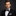 Man wearing a black suit with a white shirt and patterned bow tie on a dark background