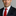 Man wearing a dark suit with a red tie against a neutral background