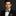 Man wearing a black suit with a plaid bow tie and pocket square on a dark background