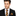 Man wearing a black suit with a blue and orange striped tie and matching pocket square on a white background