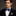Man wearing a black suit with a blue bow tie and white shirt against a dark background