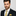 Man wearing a dark suit with a yellow tie and pocket square against a light gray background