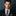 Man wearing a black suit with a purple and gray striped tie against a dark background