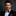 Man wearing a black suit with a purple and black plaid bow tie and pocket square on a dark background