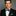 Man wearing a black suit with a green plaid bow tie and pocket square on a gray background
