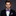 Man wearing a black suit with a red and blue checkered bow tie and pocket square on a dark background