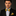 Man wearing a black suit with a yellow and blue bow tie and pocket square on a dark background