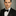 Man wearing a black tuxedo with a bow tie against a gray background