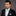 Man wearing a black suit with a light green bow tie and pocket square on a gray background
