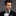 Man wearing a black suit with a patterned bow tie against a gray background