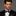 Man wearing a black suit with a patterned blue, red and gold paisley bow tie against a gray background