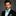 Man wearing a black suit with a white shirt and turquoise bow tie on a gray background