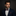 Man wearing a navy suit with a white shirt and red polka dot bow tie and pocket square against a dark background