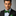 Man wearing a black suit with a green and red polka bow tie featuring red polka dots on a gray background