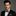 Man wearing a black suit with a checkered bow tie and pocket square on a gray background