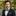 Man wearing a navy suit with a yellow polka dot bow tie and pocket square, standing outdoors.