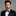 Man wearing a black suit with a green polka dot bow tie and pocket square on a gray background