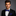 Man wearing a black suit with a blue polka dot bow tie and pocket square on a gray background