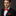 Man wearing a black suit with a red polka dot bow tie and pocket square on a dark background
