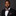 Man wearing a black suit with a patterned burgundy and black paisley bow tie and pocket square on a dark background