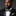 Man wearing a black suit with a patterned green and burgundy paisley bow tie and pocket square on a dark background