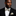 Man wearing a black suit with a patterned light blue paisley bow tie and pocket square on a gray background