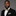 Man wearing a black suit with a gold bow tie and pocket square on a gray background