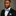 Man wearing a black suit with a blue stripe bow tie and pocket square on a gray background
