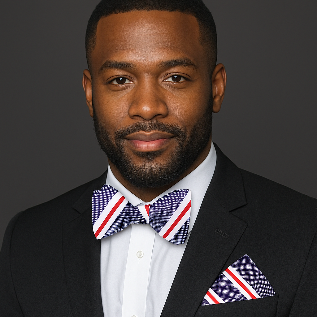 Man wearing a suit with a blue, white and red stripe patterned bow tie and pocket square on a dark background