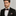 Man wearing a black suit with a black and red floral bow tie and pocket square on a gray background