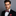 Man wearing a black suit with a red paisley patterned bow tie and pocket square on a gray background